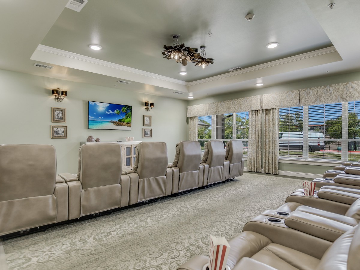 A luxurious home theater with comfortable seating, a large TV screen, and elegant chandeliers.