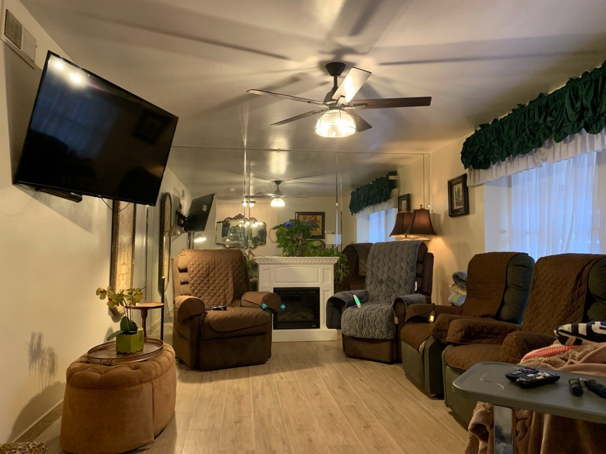 A cozy living room featuring multiple recliner chairs, a ceiling fan, and a fireplace.