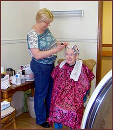 A hairdresser styling an elderly woman's hair in a comfortable indoor setting.