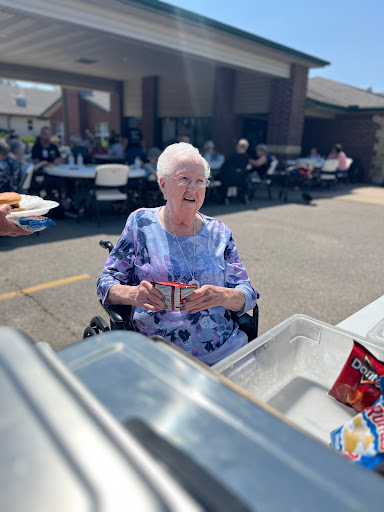 An elderly woman enjoys a sunny day at a community gathering, smiling as she receives food.