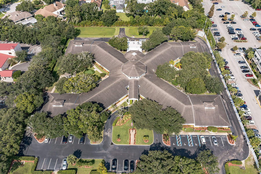 Aerial view of a cross-shaped building surrounded by trees and parking lots.