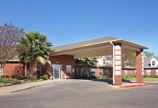 A modern building entrance with a covered walkway and palm trees under a clear blue sky.