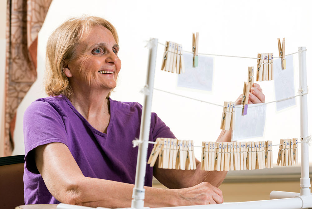 A senior woman smiling while working on a crafting project with clothespins indoors.
