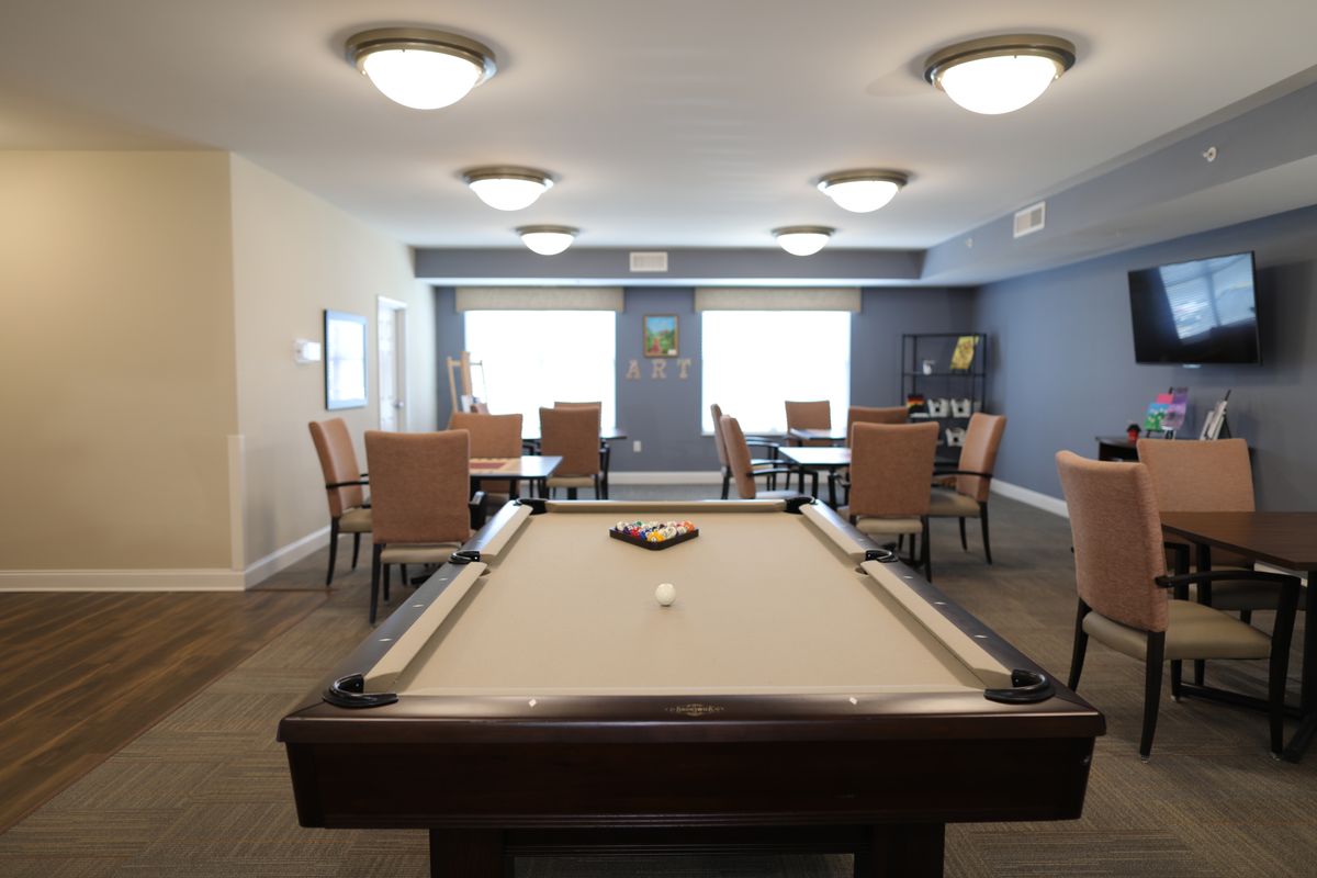 A well-lit game room featuring a pool table, chairs, and tables.