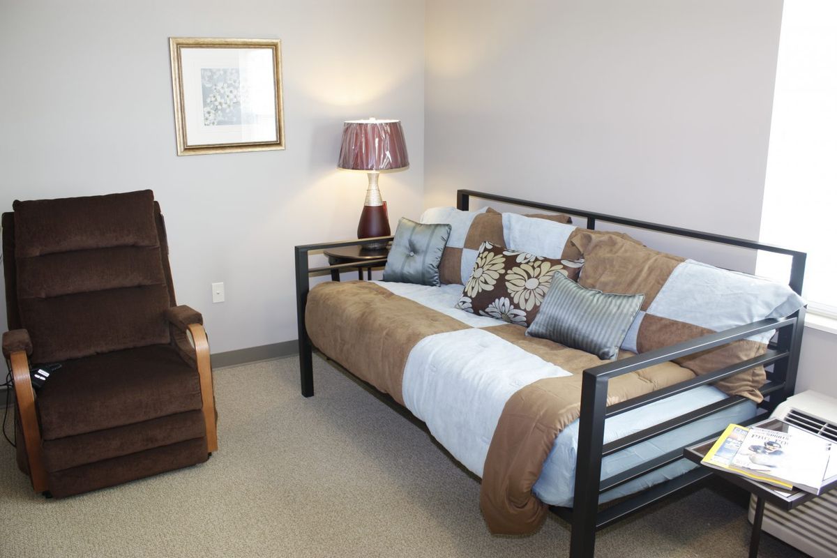 A cozy bedroom featuring a daybed with plush pillows, an armchair, and a decorative lamp.