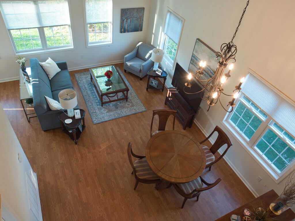 A cozy living and dining area with wooden floors, featuring a sofa, armchair, coffee table, and a round dining table beneath a chandelier.