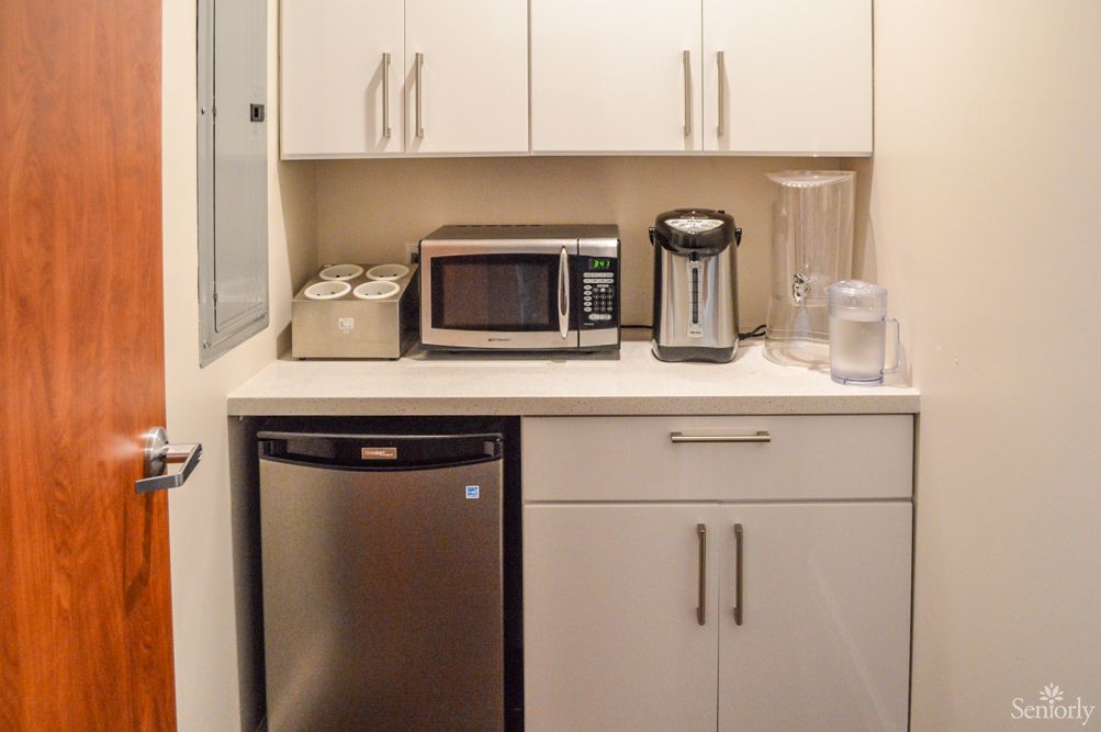A compact kitchen area featuring a microwave, coffee maker, mini fridge, and cabinet storage.