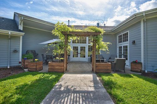 A beautiful patio area with a pergola, surrounded by greenery and outdoor seating on a sunny day.