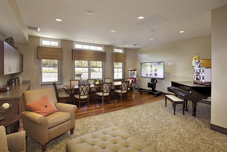 A spacious living room with a dining area, featuring elegant furniture, a grand piano, and large windows.