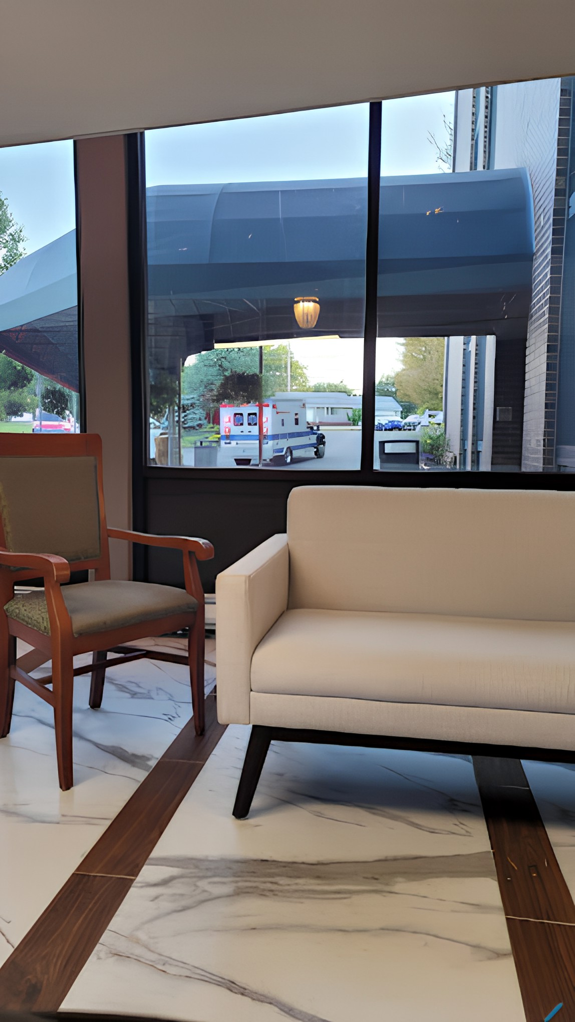A modern lobby area featuring a beige sofa and a wooden chair near large windows.