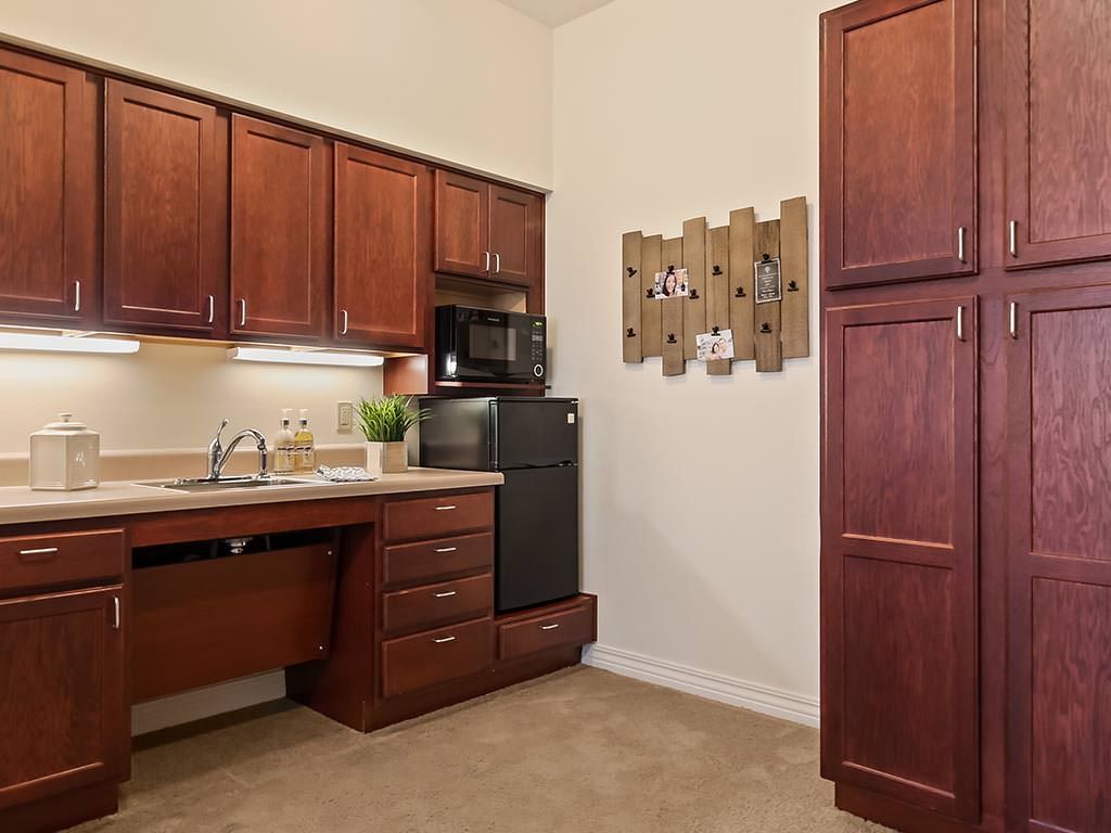 A compact kitchen area featuring wooden cabinets, a small refrigerator, microwave, and sink.