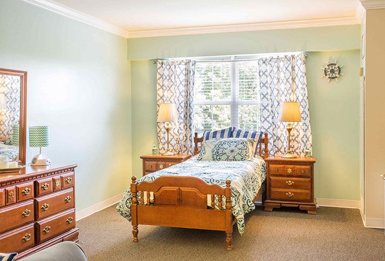 A cozy, well-lit bedroom featuring a bed with wooden frame, two nightstands, and decorative lamps by a window with patterned curtains.