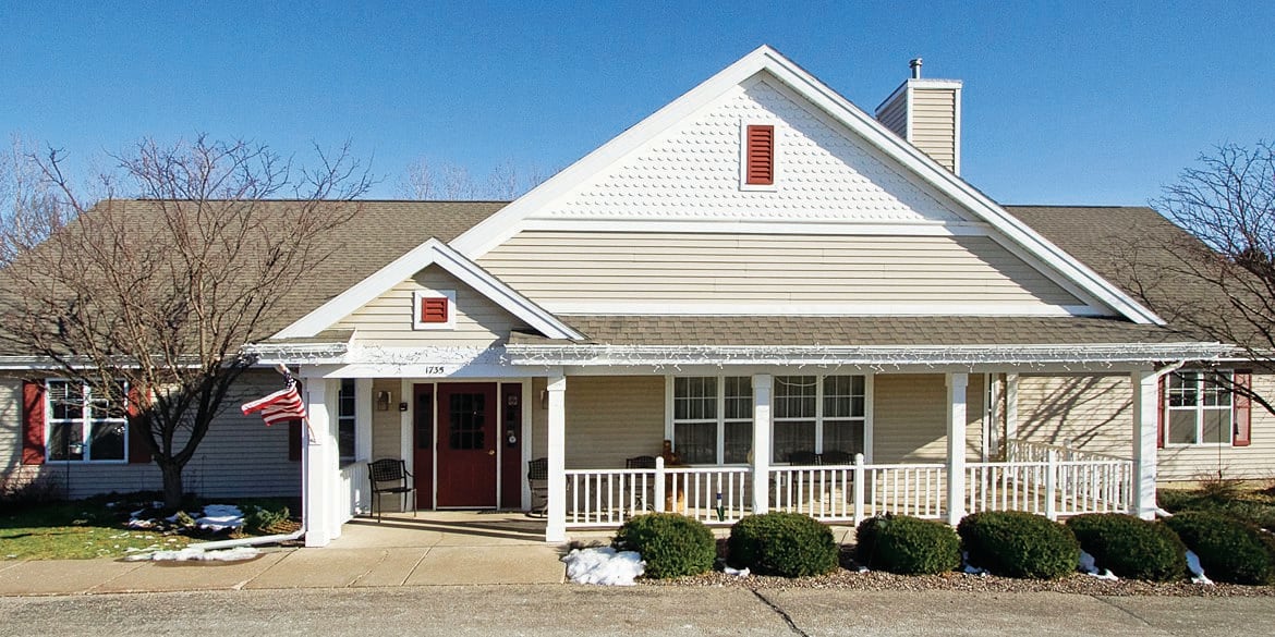 A suburban residential house with a front porch and neatly trimmed bushes.