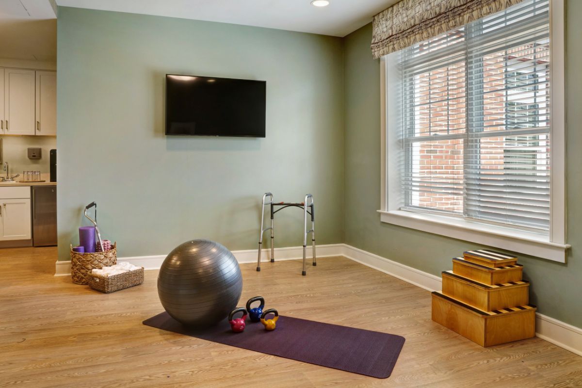 A home exercise room with fitness equipment including a yoga mat, stability ball, and kettlebells, set on a wooden floor.