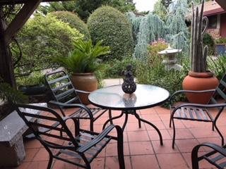 A cozy patio with a table and chairs, surrounded by lush garden greenery.