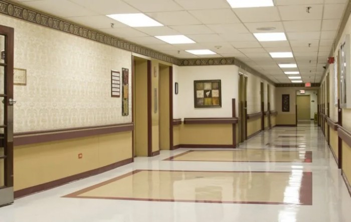 A clean hospital corridor with beige and white walls, featuring artwork and closed doors.