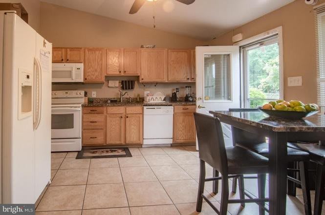 A spacious kitchen with wooden cabinets, featuring modern appliances and a dining area with an open door leading outside.