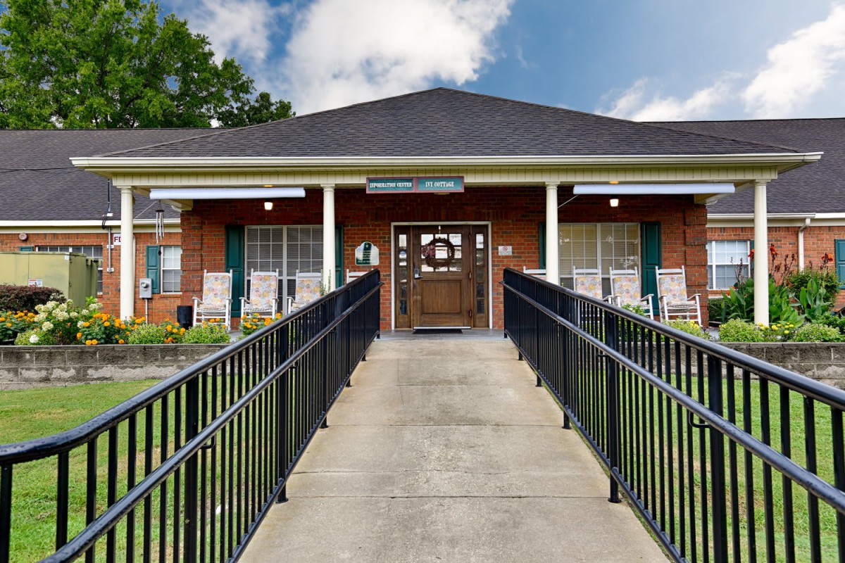 A brick building entrance with a ramp leading up to the front door, flanked by large windows.