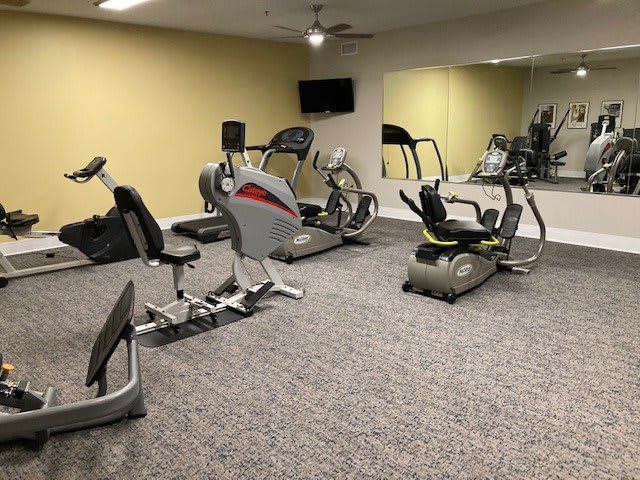 A gym room with various cardio exercise machines, including treadmills and stationary bikes, featuring a large mirror on the wall.