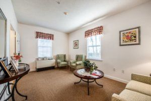 A cozy living room with two green chairs, a round coffee table, and windows with checkered curtains.