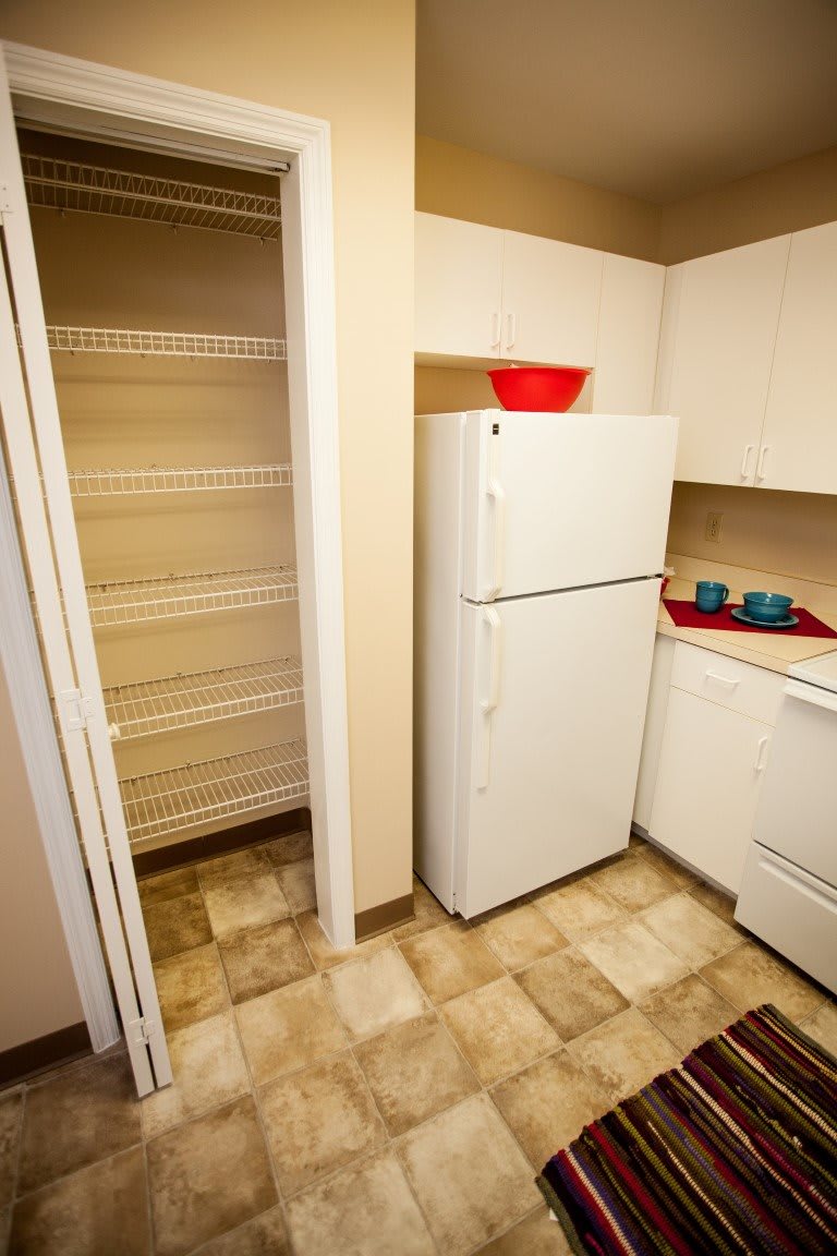 A compact kitchen with a refrigerator, pantry, and red accent decor.