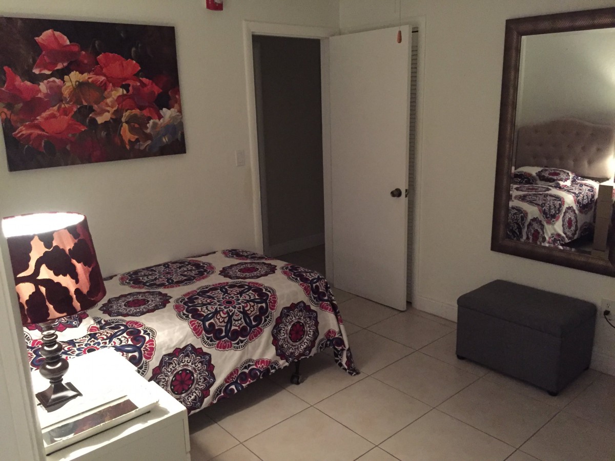 A cozy bedroom with a bed, artwork on the wall, and a large mirror.