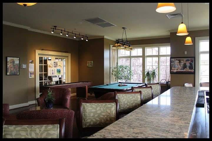 A cozy lounge area featuring a pool table and comfortable seating, illuminated by natural light from large windows.