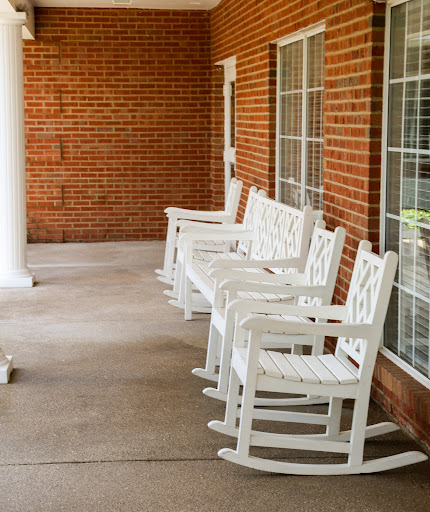 A row of white rocking chairs lined up on a porch against a brick wall, inviting relaxation.