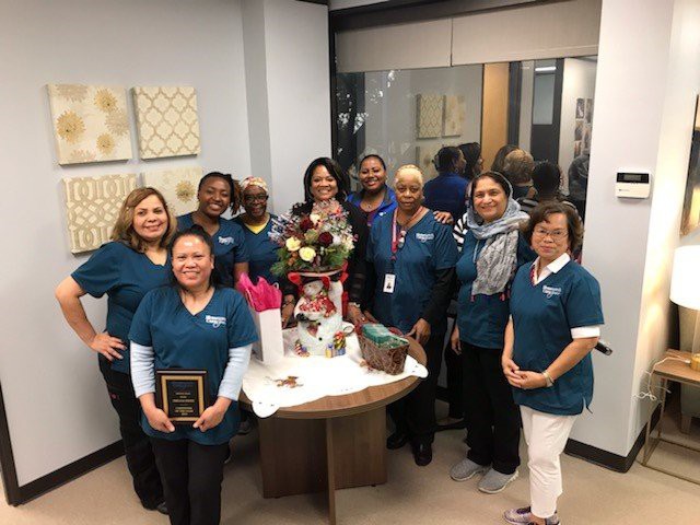 A team poses together in an office, celebrating around a decorated table.