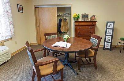 A cozy meeting room featuring a round wooden table with four chairs, a coat rack, and a floral arrangement on the table.