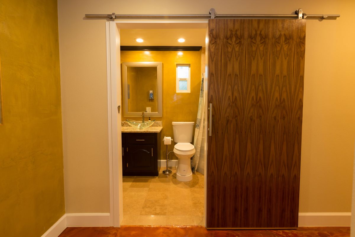 A modern bathroom with a sliding wooden door, featuring a sink, toilet, and warm lighting.