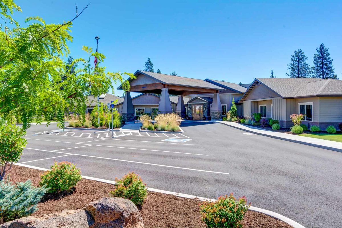 A modern building with a spacious parking area surrounded by landscaped greenery and clear blue skies.