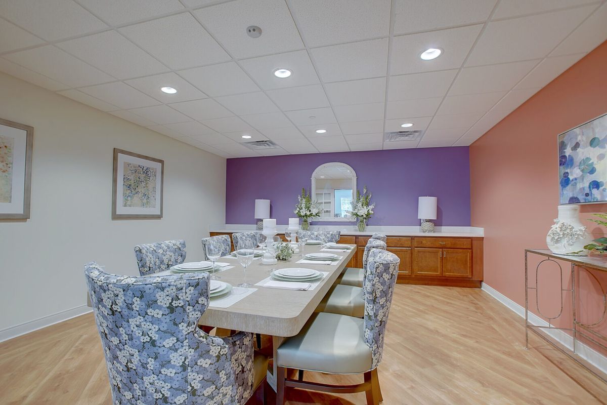 A well-decorated dining room with a long table and upholstered chairs, featuring a purple accent wall.