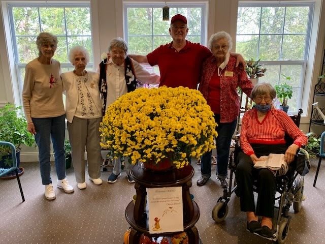 A group of seniors posing indoors with a large floral arrangement.