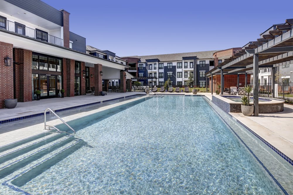 An inviting swimming pool at a modern apartment complex under a clear blue sky.