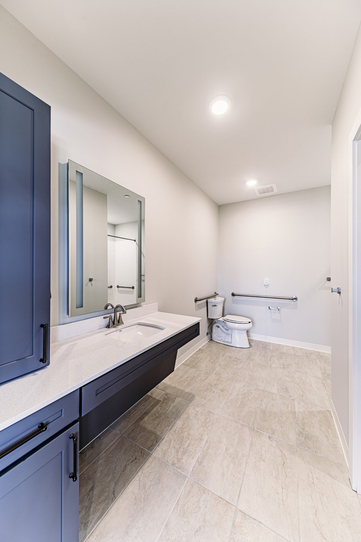 A modern, minimalist bathroom featuring a large vanity with a mirror, toilet, and ample lighting.