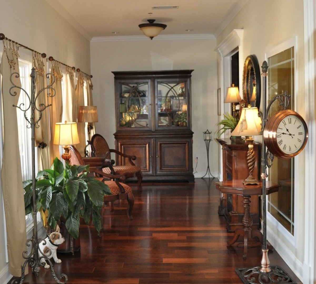 A well-decorated hallway with hardwood flooring, featuring elegant furniture, lamps, and plants.