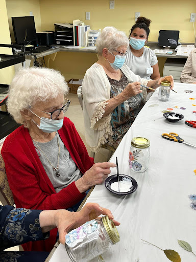 A group of elderly women engaging in a crafting activity while wearing masks.