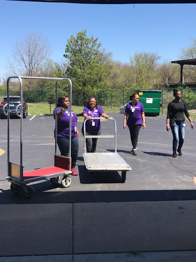 A group of individuals in purple uniforms collaborating to move equipment outside.