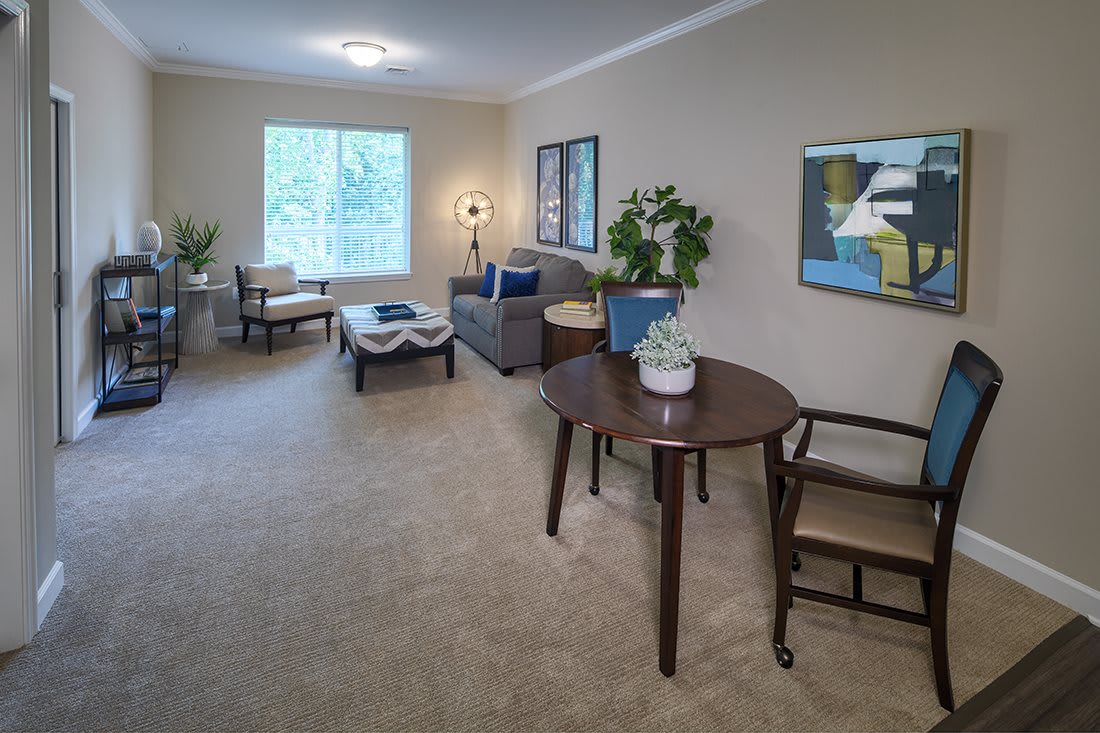 A cozy living room with modern furniture and decor, featuring a sofa, chairs, table, and artwork.