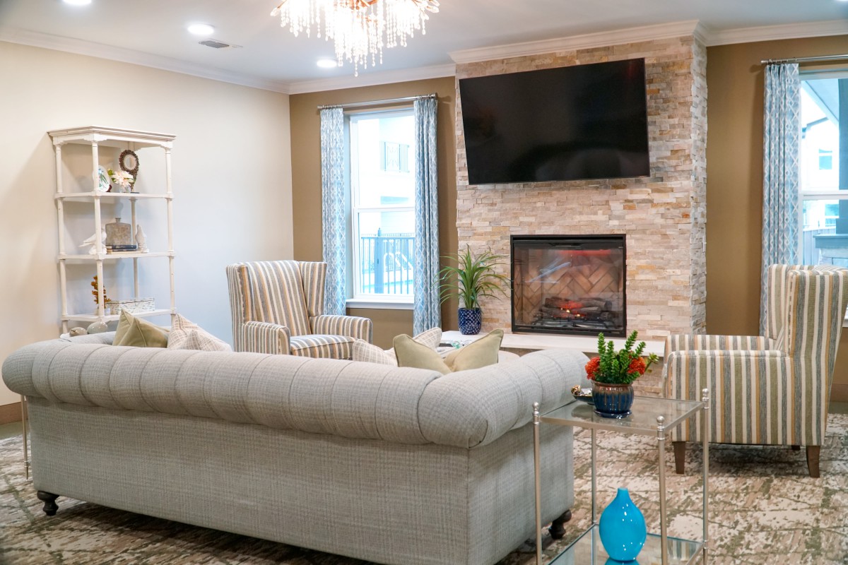 A modern living room with a comfortable sofa, stone fireplace, and a mounted television under an elegant chandelier.