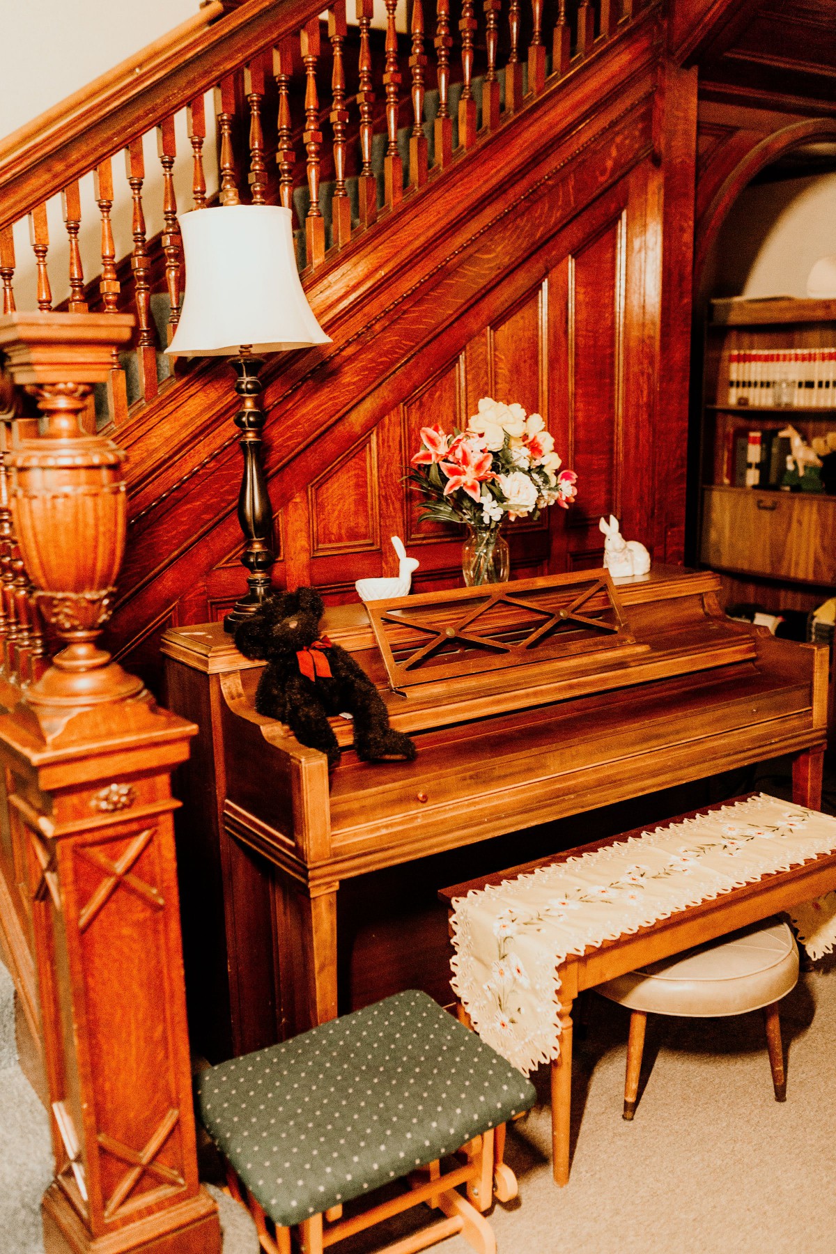 A cozy corner featuring a vintage wooden piano next to a staircase, adorned with decorative items and books.