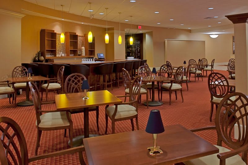 An empty restaurant bar with neatly arranged tables and chairs, soft lighting, and a cozy atmosphere.
