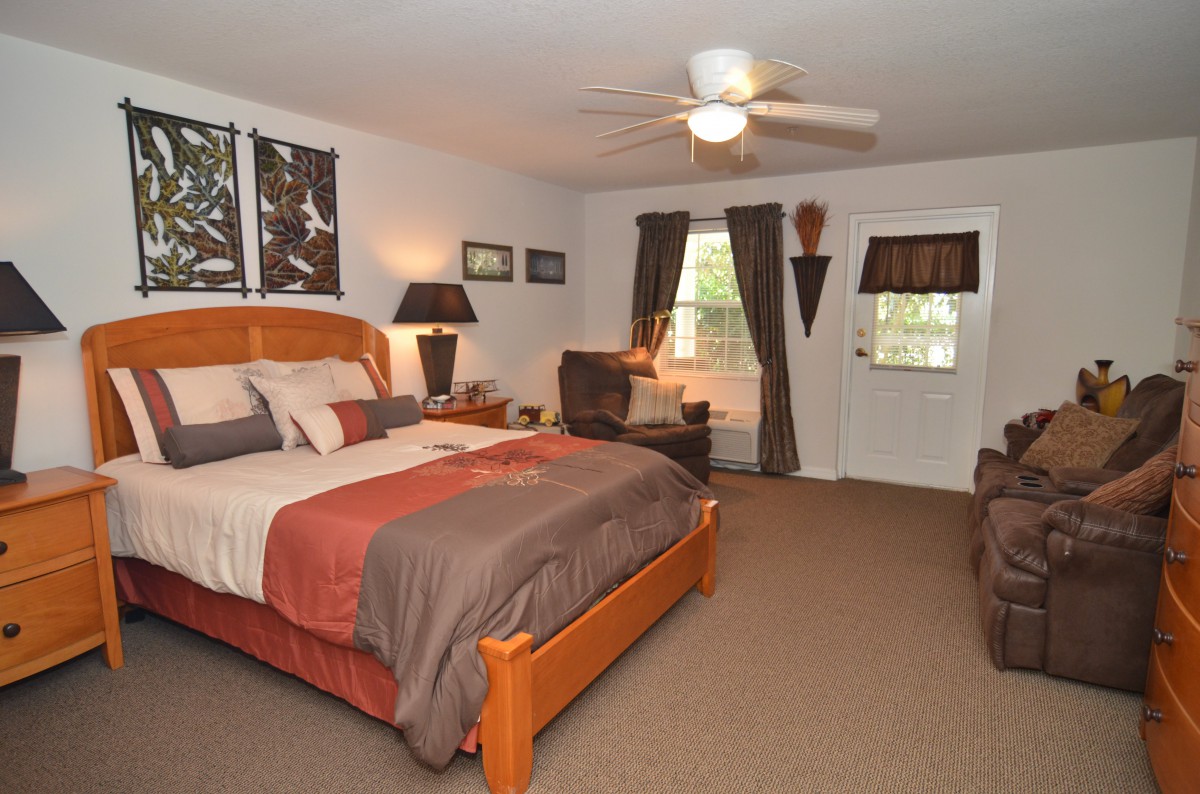 A cozy bedroom interior with a wooden bed frame, ceiling fan, and tasteful decorations.