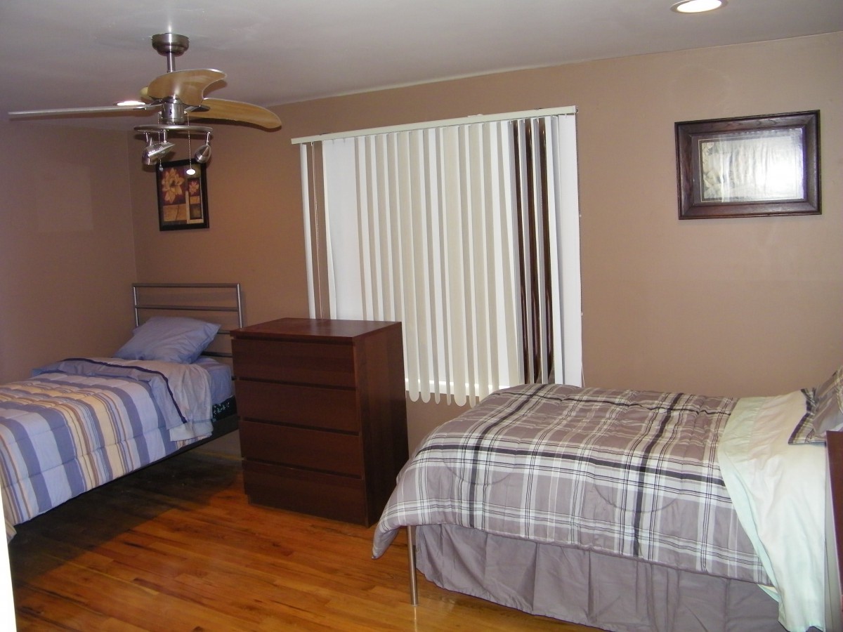 A cozy bedroom with two twin beds, a wooden dresser, and large window blinds.