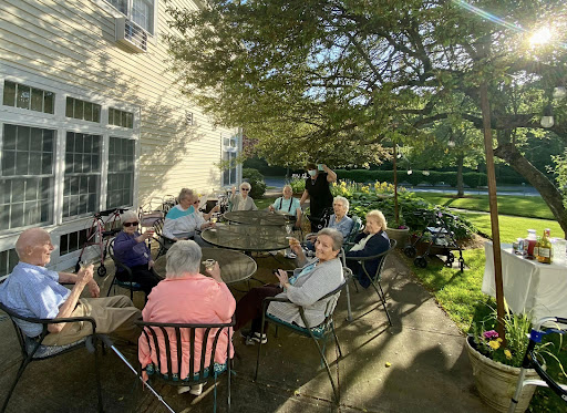 A group of seniors enjoying a sunny day outdoors, gathered around a table in a garden setting.