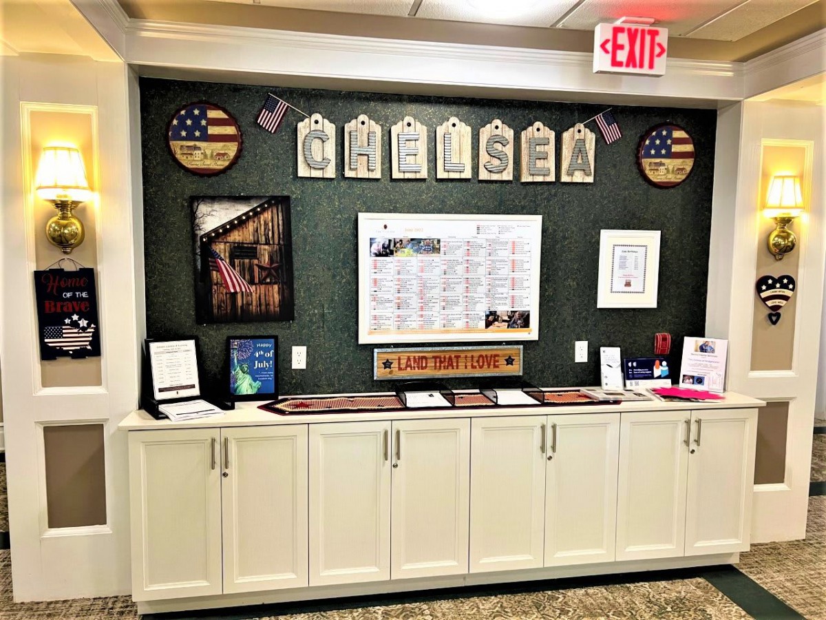 A wall display featuring patriotic decorations and a calendar above a cabinet.