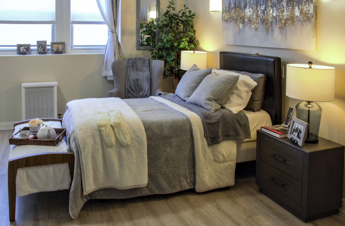 A cozy and well-decorated bedroom with a neatly made bed, soft lighting, and a lush plant by the window.