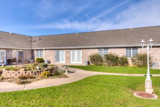 A single-story brick house with a well-maintained lawn and garden on a sunny day.