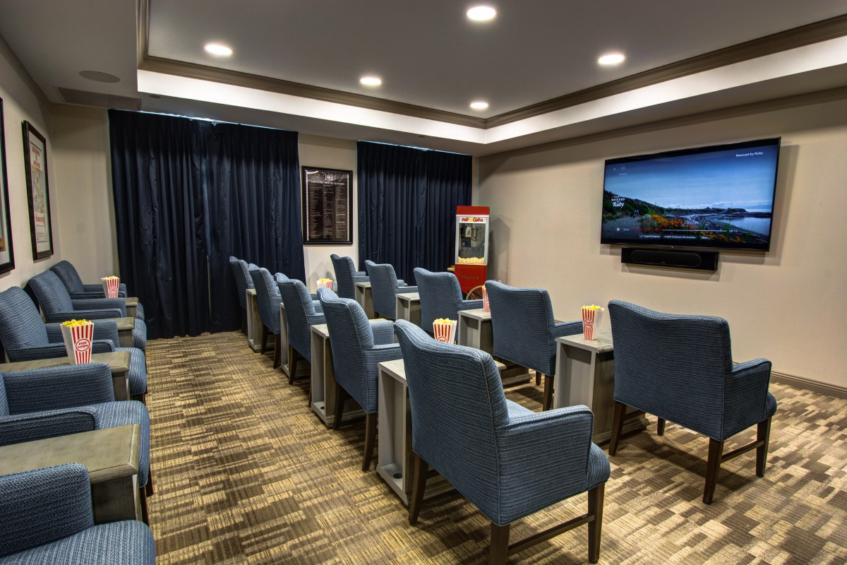 A modern theater room with rows of blue chairs facing a large screen, set up for a presentation or movie viewing.